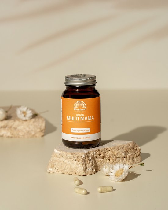 Bruine pot met oranje label: "Mattisson HEALTHSTYLE VEGAN MULTI MAMA". Twee capsules liggen voor de pot op een steen.