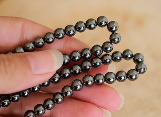 Hand houdt donkergrijze, glanzende hematiet kralenarmband vast.