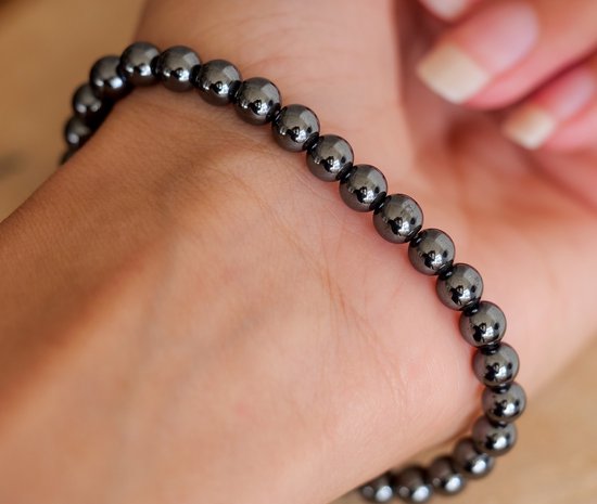 Donkergrijze, glanzende hematiet kralenarmband om een pols.