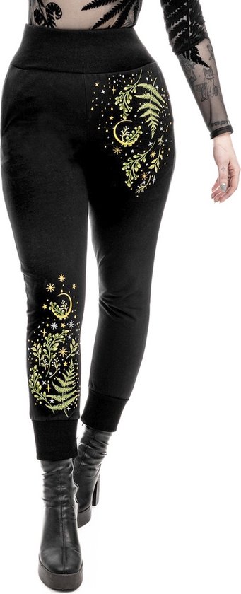 Modèle portant un pantalon noir avec des imprimés jaunes de plantes, d'étoiles et de lunes sur les jambes.