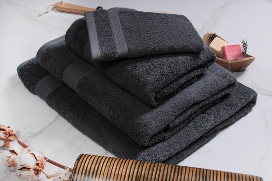 Pile de serviettes gris anthracite, avec une petite serviette posée dessus. Une coupelle en bois avec du savon et des plumes est à côté.