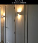 Witte wandlamp op een muur naast een deur, met een brede lichtstraal omhoog en omlaag.