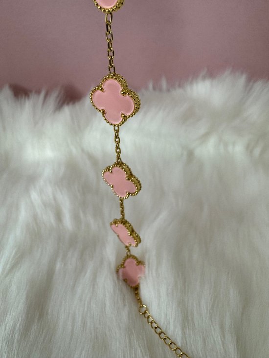 Gouden armband met meerdere roze klavervormige bedels op een zachte, witte achtergrond.