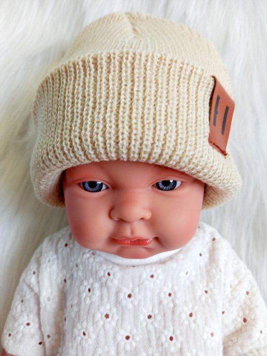Baby met crèmekleurige gebreide muts met bruin label en witte kanten top.