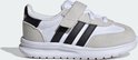 Zijaanzicht van een witte kindersneaker met grijze suède overlays, zwarte Adidas-strepen en klittenbandsluiting.