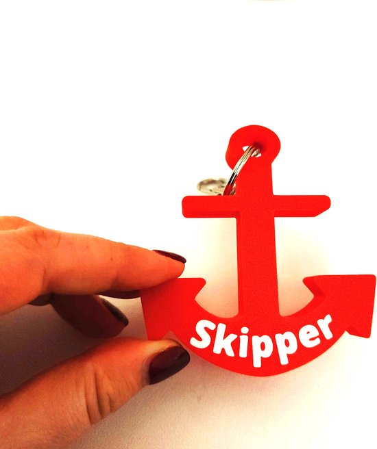 Vinger houdt rode 'Skipper' ankersleutelhanger vast. De achtergrond is wit.