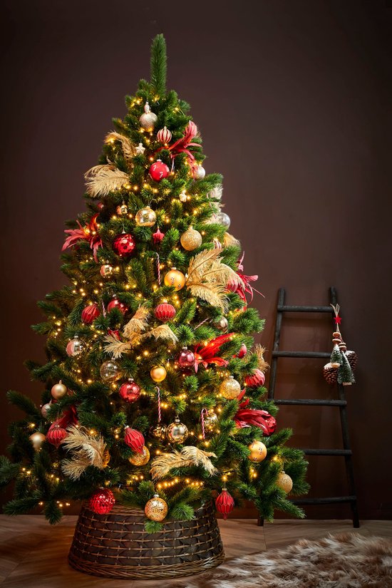 Een met kerstballen, lichtjes en veren versierde kerstboom staat naast een decoratieve zwarte ladder.