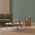 Zwart metalen nachtkastje met houtlook en twee lades in een woonkamer naast een groene bank.