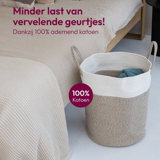 Wasmand in slaapkamer, naast bed. '100% Katoen' cirkel. Beige en witte mand met handvatten.