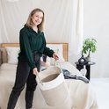 Vrouw met mand met beige en witte strepen, houdt mand met twee handen vast. Slaapkamerinterieur.