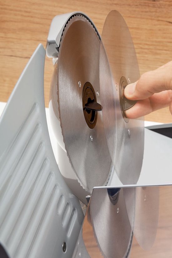 Vinger raakt een metalen snijblad aan van een zilverkleurige vleessnijmachine.