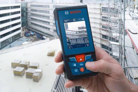 Hand die een Bosch laser afstandsmeter vasthoudt met een stadsgezicht en bouwplaats op de achtergrond.