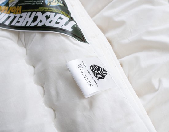 Close-up van een crème wollen dekbed met een groen 'Terschellinger Wolweelde' label en een klein wit label met 'Vulling Zuiver Scheerwol'.