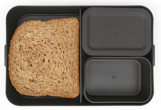 Donkergrijze bento lunchbox met een sandwich, een bakje fruit en een bakje salade, en een deksel naast de box.