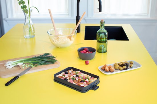 Boîte à lunch Brabantia gris foncé remplie de nourriture, sur une table de cuisine jaune.
