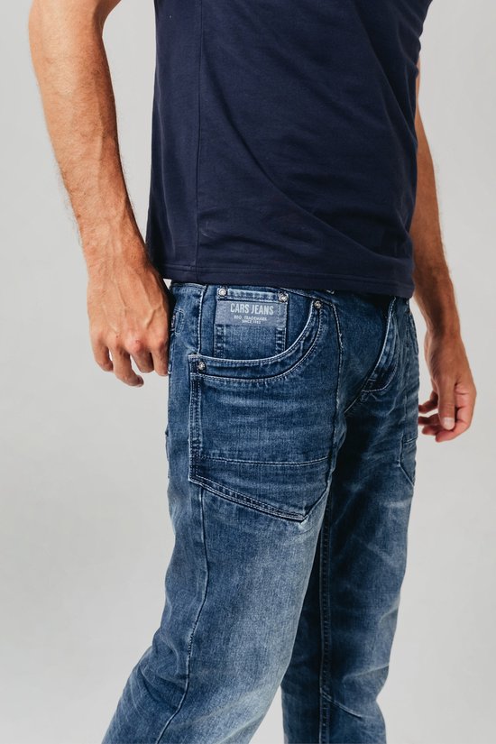 Blauwe spijkerbroek met stone wash en Cars Jeans label, gedragen door een man met een marineblauw T-shirt.