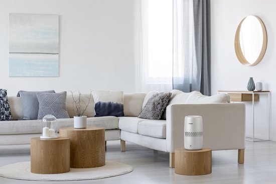 Humidificateur d'air Philips blanc sur une table d'appoint en bois dans un salon lumineux.