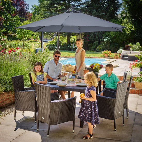 Een gezin zit aan een tafel onder een donkergrijze zweefparasol, met een zwembad op de achtergrond.