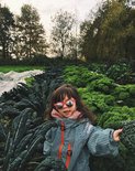Meisje met zonnebril in groen regenpak met visgraatpatroon, staand tussen kale.