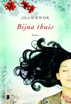 Boekomslag met de titel 'Bijna thuis'. Een close-up van een vrouw met lang, donker haar op een lichtgroene achtergrond met bloesemtakken.