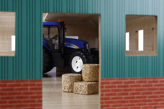 Houten landbouwloods met groene zijkanten. Een blauwe New Holland tractor en strobalen zichtbaar.