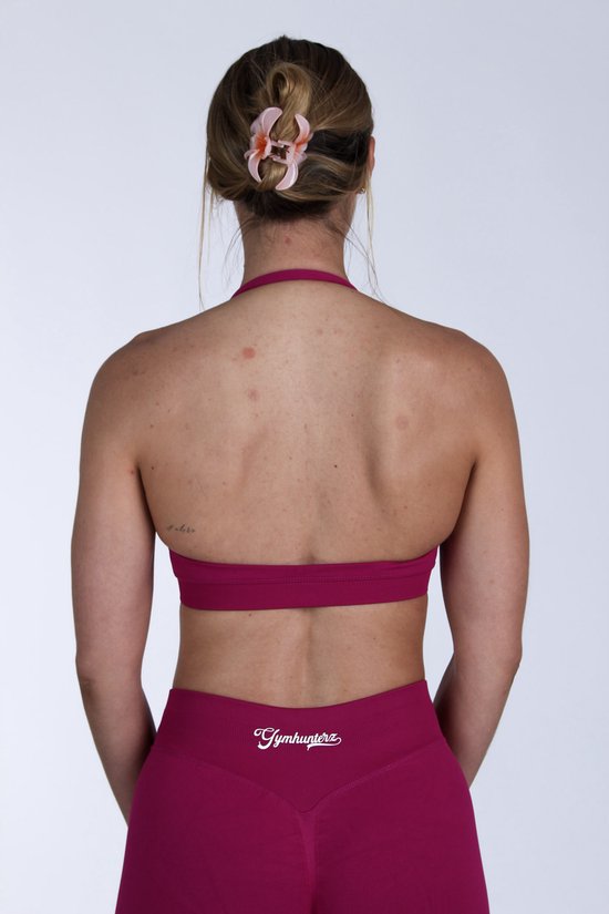 Rug van een vrouw in felroze sportbeha en short, met het 'Gymhunterz'-logo op de achterkant van de short.