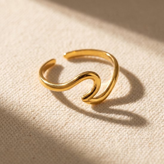 Bague dorée au design ondulé, sur une texture beige.