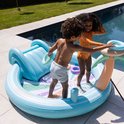 Twee kinderen spelen in een opblaasbaar zwembad met glijbaan en palmtak sproeier. Ze gooien ringen.