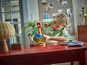 Une fille construit la figurine Heihei avec des LEGO, avec une tête rouge et des ailes et une queue bleu-vert.