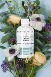 Witte fles Il Bucato di Adele 'Flower Breeze' omringd door bloemen en eucalyptus op een blauwe achtergrond.