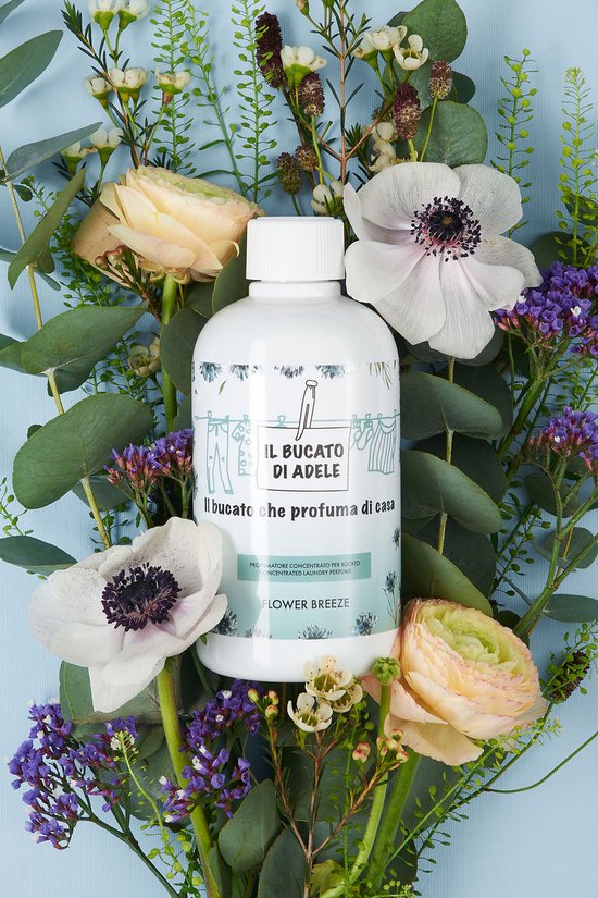 Witte fles Il Bucato di Adele 'Flower Breeze' omringd door bloemen en eucalyptus op een blauwe achtergrond.