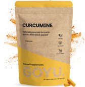 Bruine papieren zak met "CURCUMINE" en "GOYU" in gele letters, omgeven door rondvliegend kurkumapoeder. Twee oranje capsules liggen ernaast.