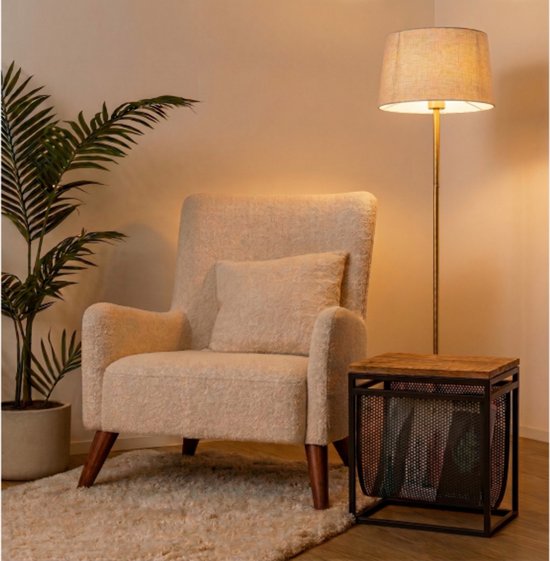 Gezellige woonkamer met zandkleurige fauteuil, bijzettafel met houten blad en zwart metalen mand, en een staande lamp.