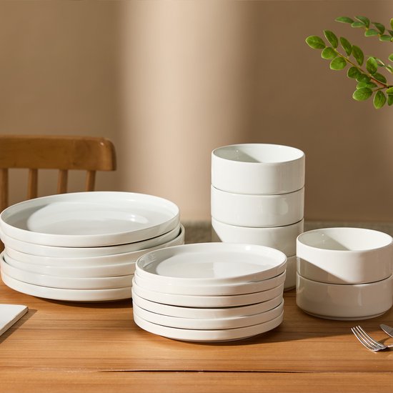 Stapel witte borden en kommen op een houten tafel, klaar voor gebruik.