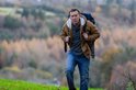 Nicolas Cage draagt een rode jas, grijs vest en spijkerbroek met een rugzak.