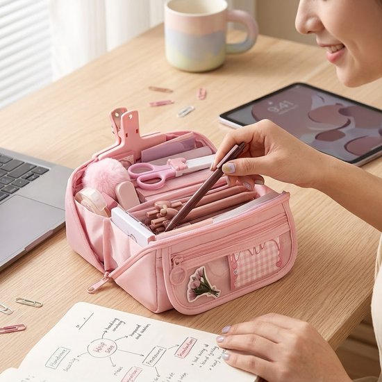 Roze etui met dubbele rits, gevuld met pennen, schaar en andere kantoorspullen. Een hand pakt een pen uit de etui. Voorvak met ruitjes en bloemdecoratie.