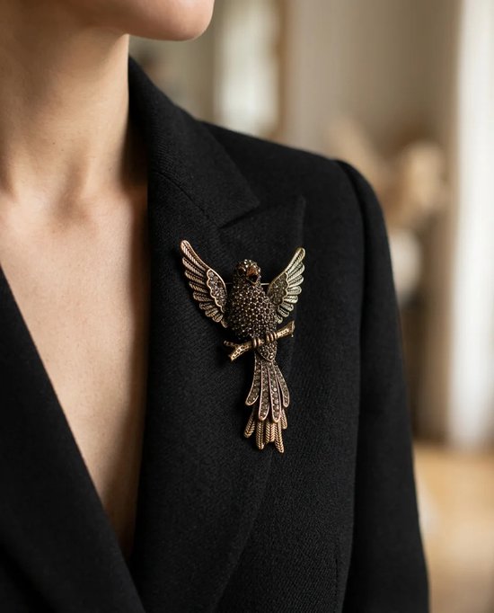 Bronzen vogelbroche met zwarte kristallen, gedragen op de revers van een elegant zwart jasje.
