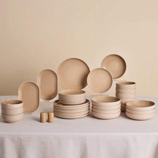 Een complete crème-kleurige aardewerken servies set met diverse borden, kommen, ovenschalen en zoutvaatjes.