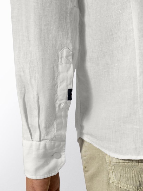 Detail van de mouw en zijnaad van een wit linnen overhemd met label.