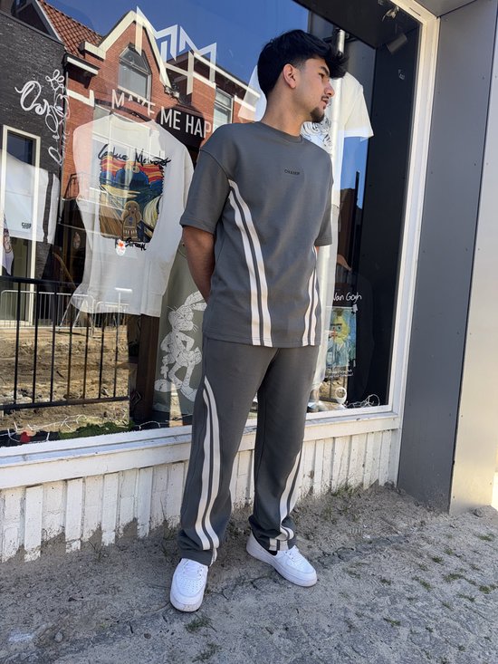 Man in donkergrijs trainingspak met witte strepen op de zijkant van de broek en mouw.