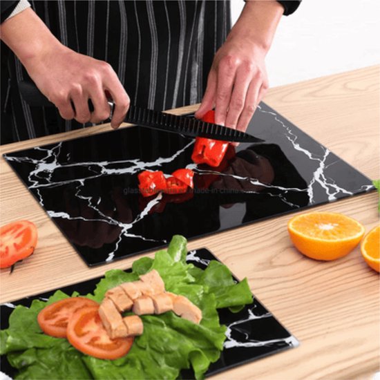 Planche à découper en verre noir à motif marbré, avec une personne coupant du poivron rouge.