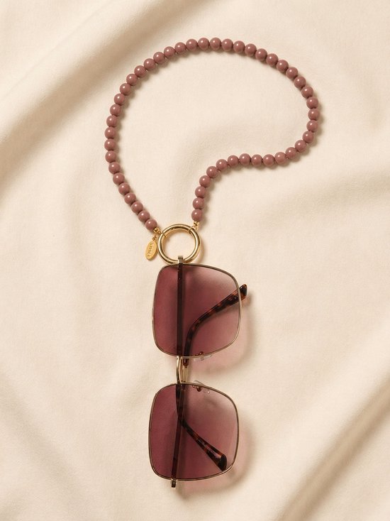 Lichtbruine kralen ketting met gouden ring, verbonden aan een vierkante zonnebril met bruine glazen.