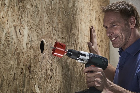 Man boort een gat in een houten plaatmateriaal met een rode Wolfcraft-gatenzaag en een boormachine.