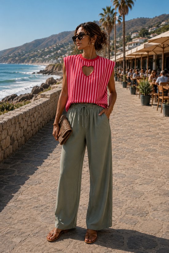 Model in een rood-roze gestreepte top met schouderpads en een hartvormige uitsnijding, gecombineerd met een olijfgroene wijde broek.