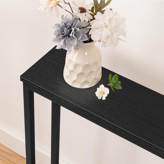 Zwarte consoletafel met een witte vaas met bloemen, een kleine witte bloem en een groen blaadje.