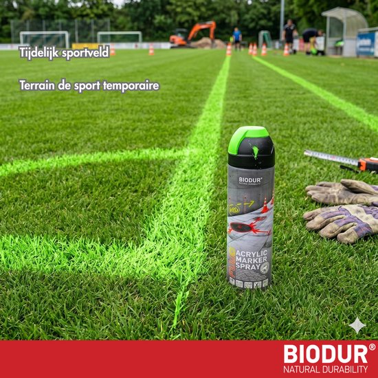 Groene spuitbus op een grasveld met gemarkeerde lijnen en een graafmachine op de achtergrond.