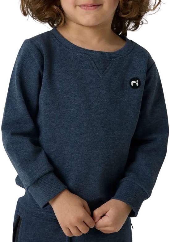 Jongetje met krullend haar draagt een donkerblauwe sweater met een geborduurd logo op de borst.