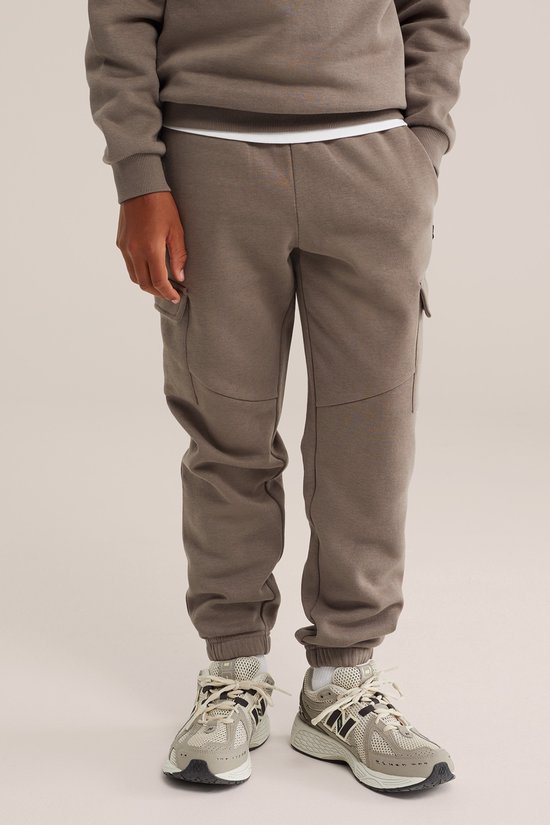 Jongens broek in bruine kleur. De broek heeft cargo zakken, elastische enkelbanden en schoenen met witte en grijze accenten.