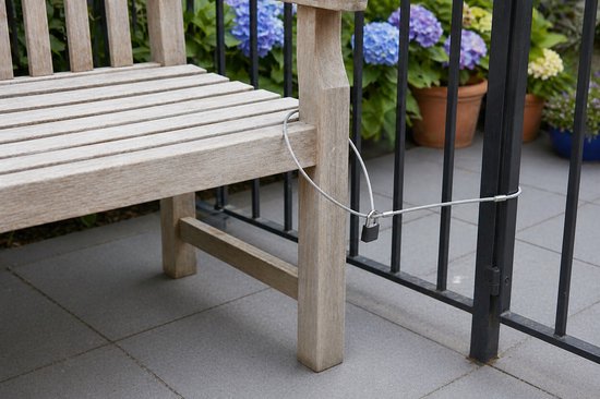 Zilveren staalkabel met zwart hangslot om een houten bankje aan een hek te beveiligen.