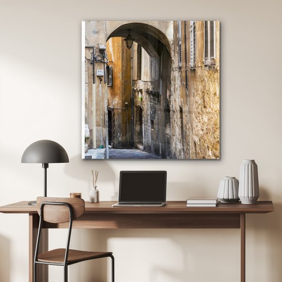® Glasschilderij 90x90 cm - Schilderij acrylglas - Stenen boog in een steegje tijdens een zonnige dag - Foto op glas - Muurdecoratie woonkamer - Wanddecoratie slaapkamer - Schilderijen